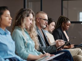 Mature man in eyeglasses filling the form before interview while sitting in waiting room among other candidates