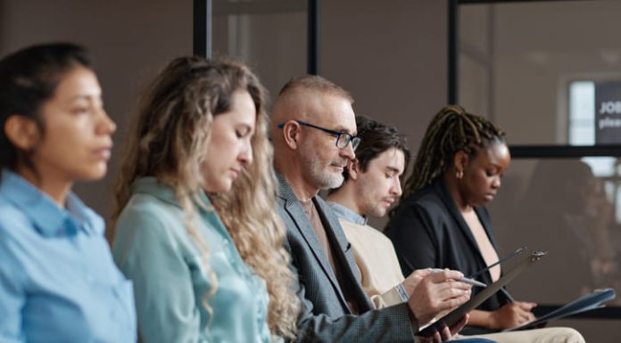 Mature man in eyeglasses filling the form before interview while sitting in waiting room among other candidates