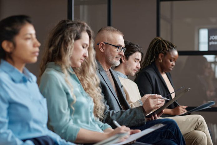 iStock-1393635743 (1) Mature man in eyeglasses filling the form before interview while sitting in waiting room among other candidates