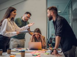 Stressed annoyed office employee manager having headache migraine at business meeting with his colleagues about business problem they have to solve.