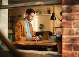 How to Balance Privacy and Productivity in Remote Work Monitoring Handsome Man Typing on Laptop Computer in Loft Apartment, Sunny Day Outside. Creative Male Checking Social Media, Browsing Internet. Productivity in Working From Home.