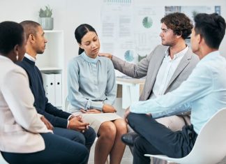 Diverse colleagues support and comfort unhappy, sad, emotional well-being coworker at team meeting or gathering. Compassionate, caring employees showing empathy to distressed woman