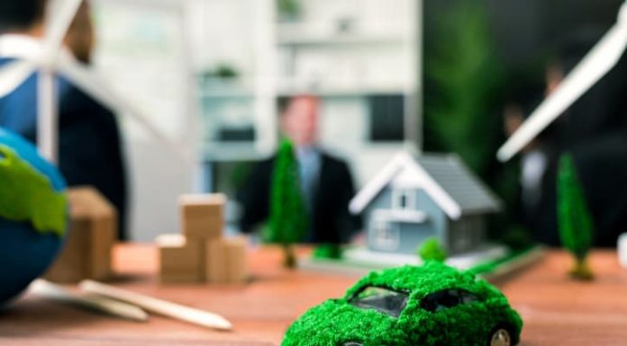 EV car model on table with blurred business people planning business marketing for eco-friendly car in background. Greener future with alternative energy charge utilization in business