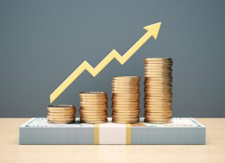 Yellow bullish arrow indicator bar chart design with stacks of coins stacked on top of 100 dollar bill on wooden background. money rise for Investor