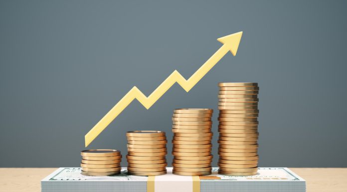 Where the Ultra-Rich Are Stashing Cash Now (Not Crypto) Yellow bullish arrow indicator bar chart design with stacks of coins stacked on top of 100 dollar bill on wooden background. money rise for Investor