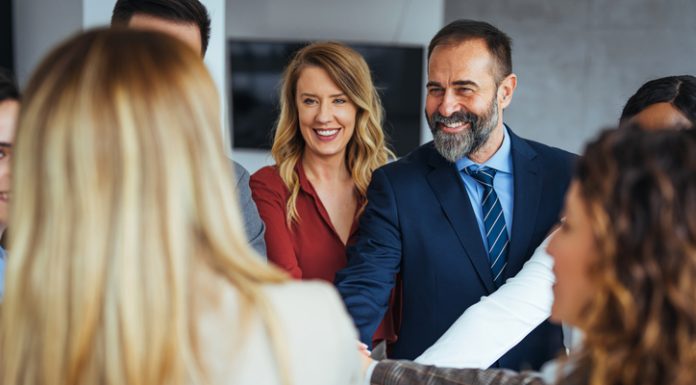 A diverse business team smiling and joining hands in a show of unity, care and teamwork.
