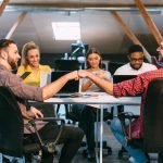 Two team members trusting each other while shaking hands while seated at a conference table surrounded by colleagues in a contemporary office environment.