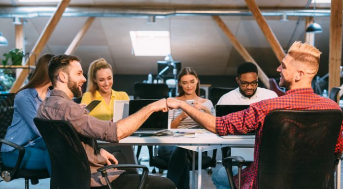 Two team members trusting each other while shaking hands while seated at a conference table surrounded by colleagues in a contemporary office environment.