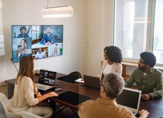 Leading Hybrid Teams By Fostering Trust Across Boundaries Business professionals actively discussing ideas and strategies during a hybrid corporate meeting.