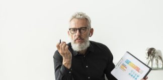 Older man at home showing graph on notepad with tablet on desk for traditional budgeting