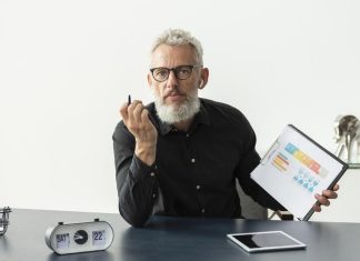 Older man at home showing graph on notepad with tablet on desk for traditional budgeting