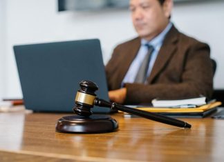 Seven Questions to Ask Your Personal Injury Lawyer A male lawyer in a brown suit on his computer typing with a gavel front and center on his desk.