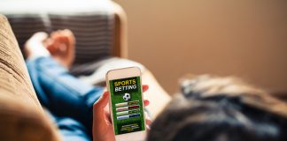 Woman holding a mobile phone with sports betting match on website app in the screen.