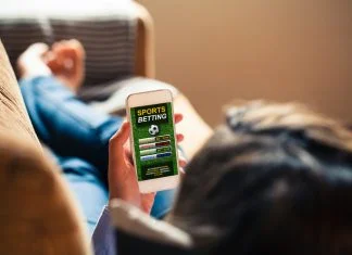 Woman holding a mobile phone with sports betting match on website app in the screen.