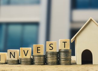 Wooden block on stacked coins with wooden house model. Depicts the growth of the real estate business.