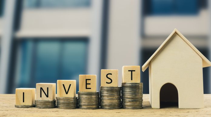 Why Invest in Real Estate & How to Do It Wooden block on stacked coins with wooden house model. Depicts the growth of the real estate business.