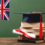 Books, academic cap, diploma and UK flag on wooden surface isolated on green