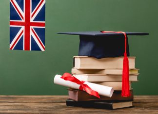 Books, academic cap, diploma and UK flag on wooden surface isolated on green