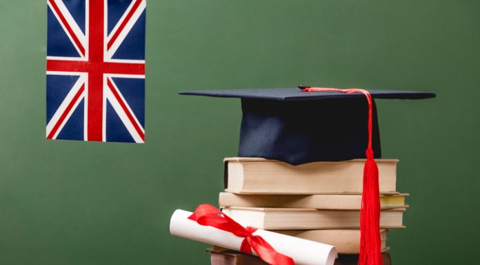 Books, academic cap, diploma and UK flag on wooden surface isolated on green