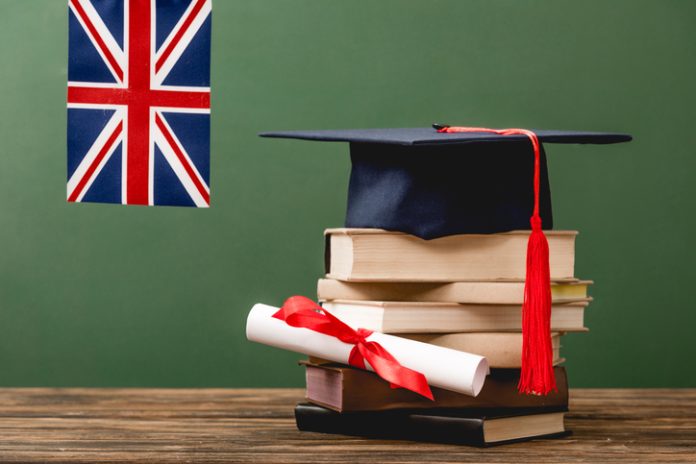 Books, academic cap, diploma and UK flag on wooden surface isolated on green