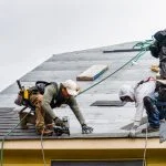 More Than Shelter: How a Quality Roof Safeguards Your Home, Saves Energy, and Increases Property Worth Crew Installing New Shingles on Roof on a Rainy Day