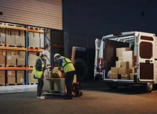 Outside of Logistics Retailer Warehouse With Female Manager Using Tablet Computer, Worker Loading Delivery Truck with Cardboard Boxes and materials