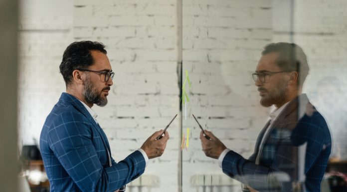 How Does Self-Reflection Fuel Stronger Leadership? Businessman holding a pen looking at himself in the mirror