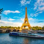 The main attraction of Paris and all of Europe is the Eiffel tower in the rays of the setting sun on the bank of Seine river with cruise tourist ships. Promoting tourism