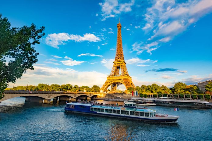 iStock-2052531938 (1) The main attraction of Paris and all of Europe is the Eiffel tower in the rays of the setting sun on the bank of Seine river with cruise tourist ships. Promoting tourism