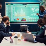 How to Calculate Market Share? Startup team analyzing worldwide sales, shares and client feedback, using interactive boar to examine revenue and funds.