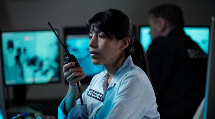 Security officer of surveillance room reporting situation on walkie-talkie while looking at computer screen
