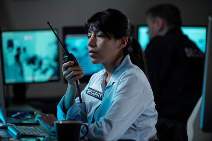 Security officer of surveillance room reporting situation on walkie-talkie while looking at computer screen