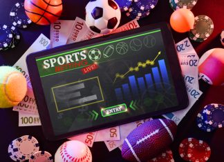Online sports betting, fan with tablet with application in the center of a black table with objects representative of different sports, money and betting chips.