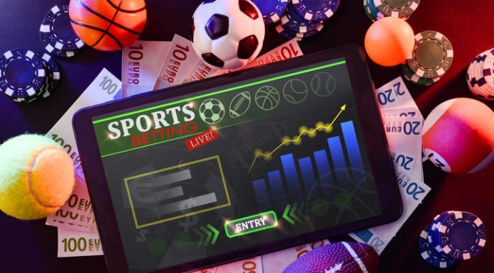 Online sports betting, fan with tablet with application in the center of a black table with objects representative of different sports, money and betting chips.