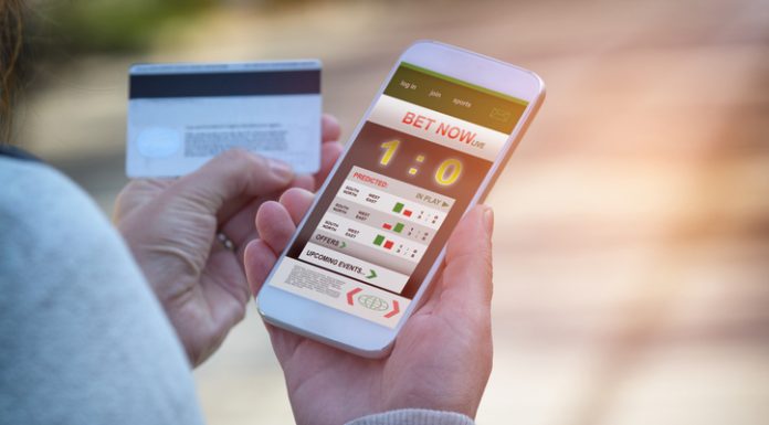 Man betting on sports, holding smart phone with working online betting mobile application