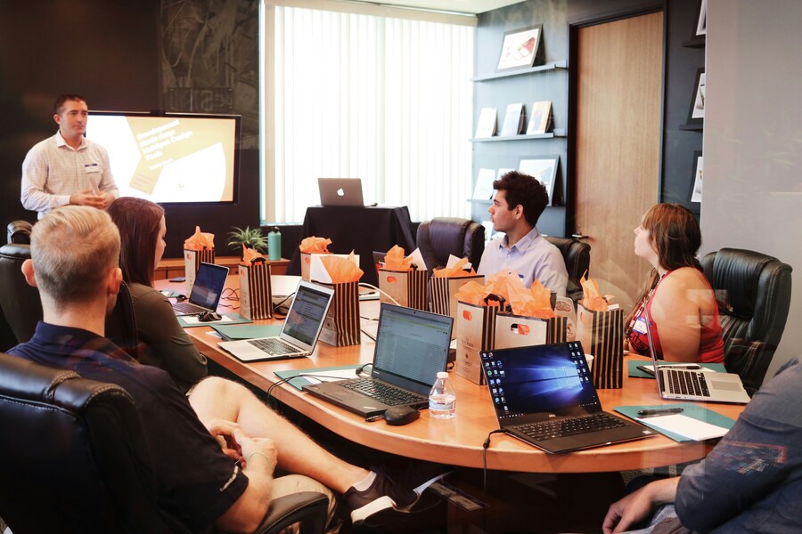 Man standing in front of people sitting beside table with laptop and computers