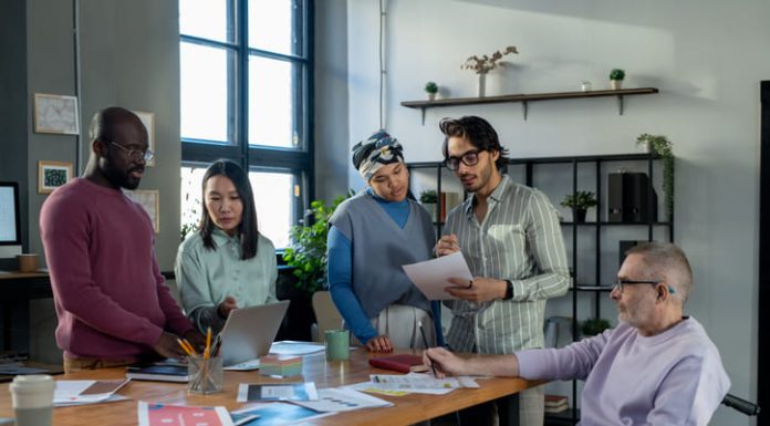 We’ve Made Space for Neurodivergence – But the Mission Is Far from Over Large group of intercultural colleagues, neurodiverse discussing online financial data and papers while standing by workplace in urban office