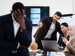 How to Handle a Toxic Colleague – Strategies to Protect Your Wellbeing group of business people pointing and talking rumor spread behind stress colleague at workplace, diverse coporate employee gossip and bully black person while meeting in financial office.