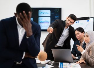 group of business people pointing and talking rumor spread behind stress colleague at workplace, diverse coporate employee gossip and bully black person while meeting in financial office.