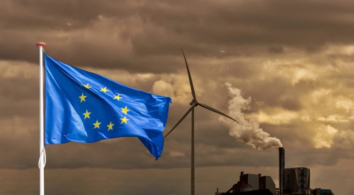The Role of Policy in a Competitive, More Resilient Europe Waving flag of Europe in front of a polluting factory chimney with smoke and wind turbine