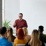 Corporate speaker delivering a motivating training about affirmation to a group of diverse employees.