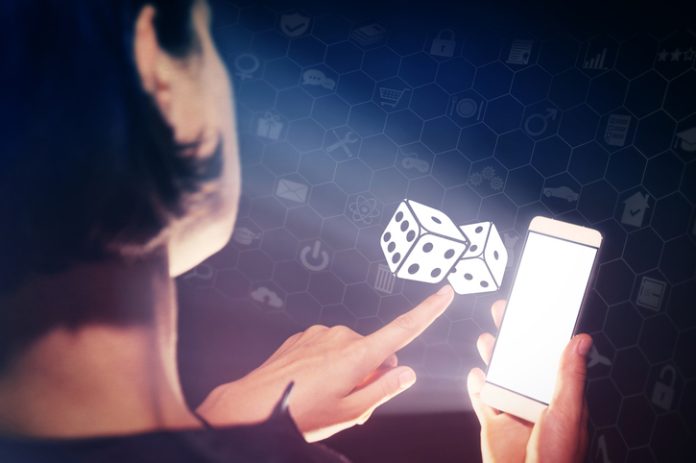 Image of a girl with a smartphone in hands. She presses on the dice icon. Concept of entertainment and iGaming