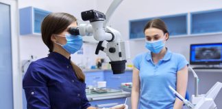 Professional dentist treats teeth using dental microscope and tools.