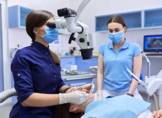 Professional dentist treats teeth using dental microscope and tools.