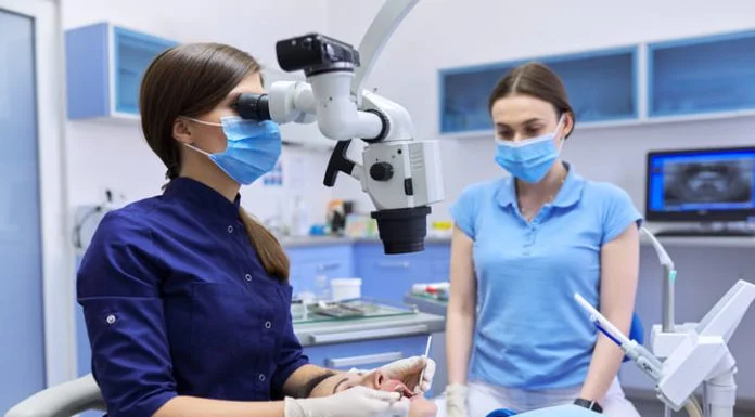 Professional dentist treats teeth using dental microscope and tools.