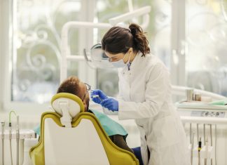 A female dentist is working with patient and fixing bad tooth while standing at dentist office.