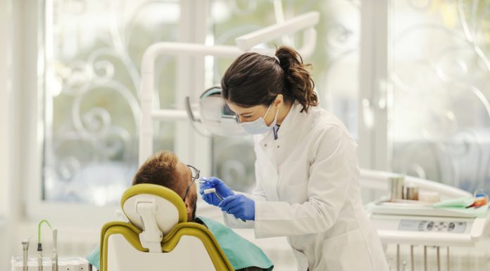 A female dentist is working with patient and fixing bad tooth while standing at dentist office.