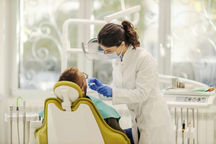 Dentist is fixing tooth while standing at the dentist office with her patient. A female dentist is working with patient and fixing bad tooth while standing at dentist office.
