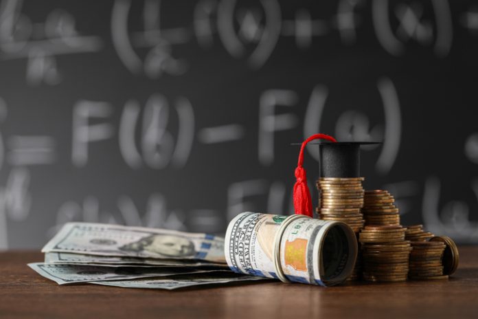 Coins, MBA ROI, dollar banknotes and graduation cap on wooden table