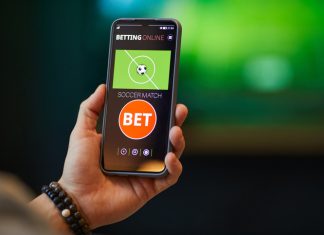 Close-up of hand holding smartphone with soccer betting app interface showing bet options and match information in background